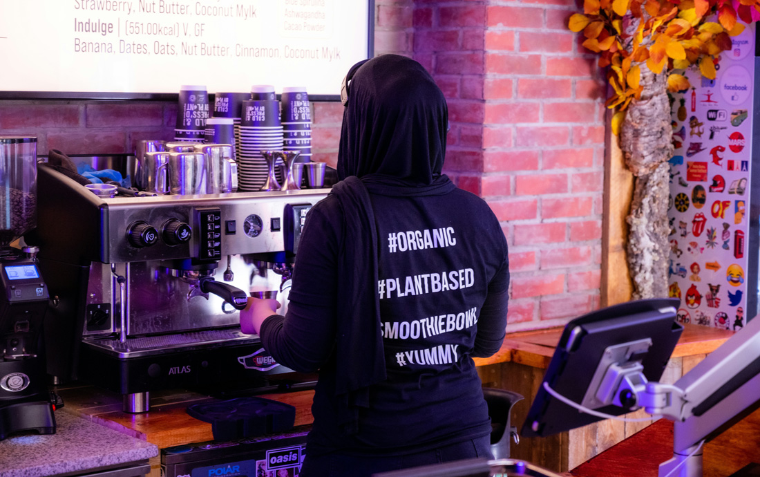 Person steht vor Kaffeemaschine, verschiedene Hashtags auf dem Pullover